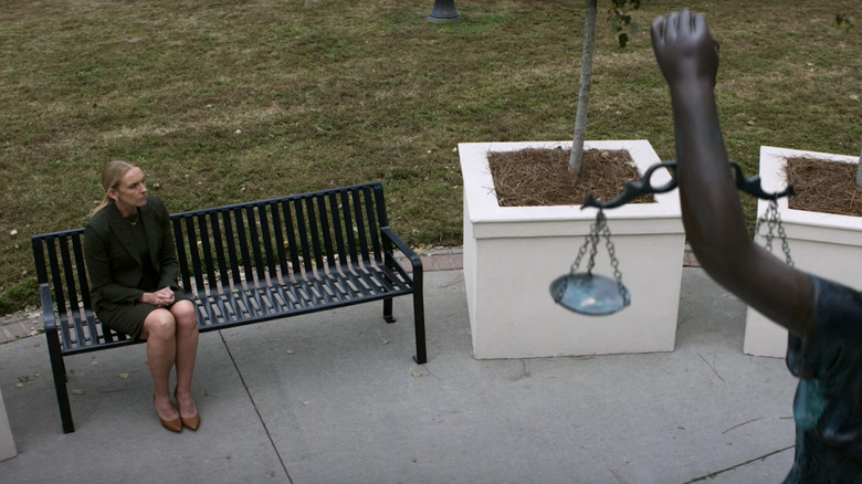 Toni Collette's Faith Killebrew sits on a bench with the scales of justice visible in the foreground in Juror #2