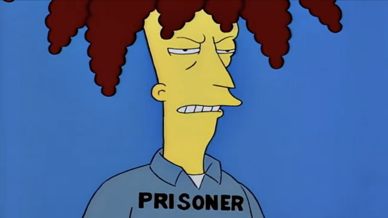 Sideshow Bob looks angry as he stands against a blue background and wears a costume that says Prisoner from The Simpsons.