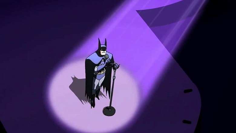 Batman stands on a stage singing
