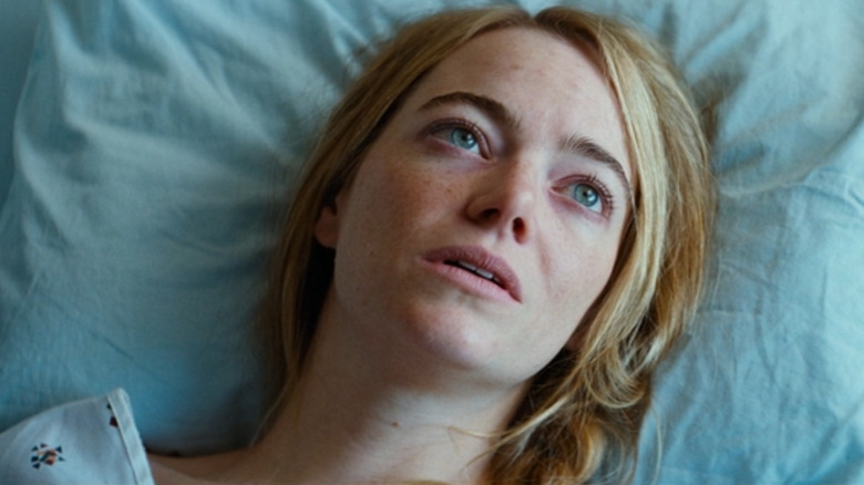 Emma Stone as Liz in Kinds of Kindness, lying in a hospital bed