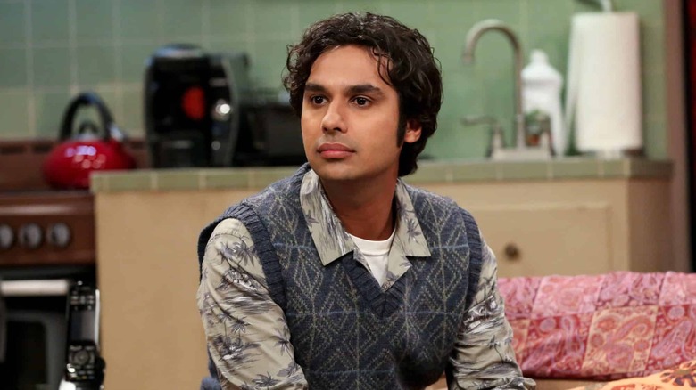 Raj sitting at a table in a kitchen wearing a sweater vest on The Big Bang Theory