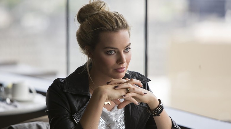 Margot Robbie como Jess sentada em uma mesa em Focus