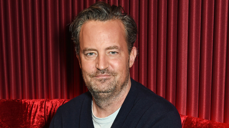 Matthew Perry sitting on red velvet couch