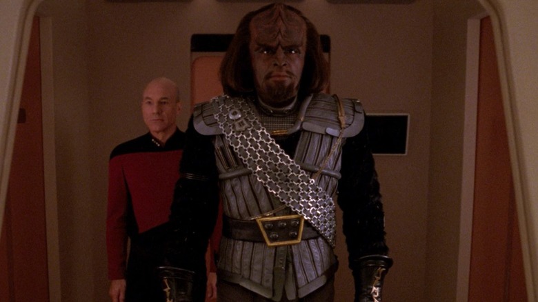 Worf, in full Klingon regalia, walking down a corridor, Captain Picard behind him.