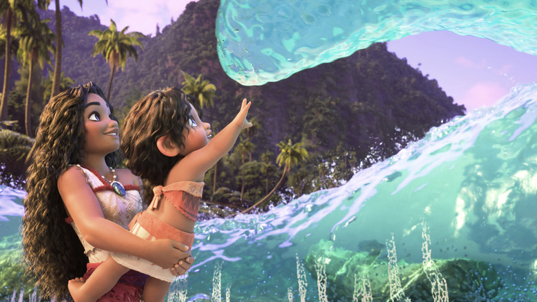 Moana sostiene a su hermana pequeña Simia mientras alcanza las olas del océano en Moana 2.