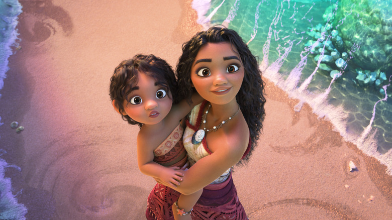 Auli'i Cravalho as Moana holding Khaleesi Lambert-Tsuda as Simea looking upward on the beach in Moana 2