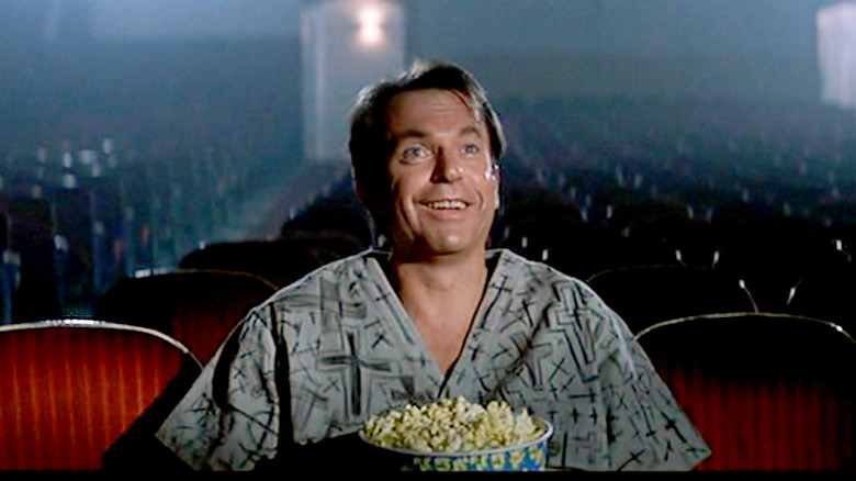 man smiling alone in a movie theatre with popcorn in his lap