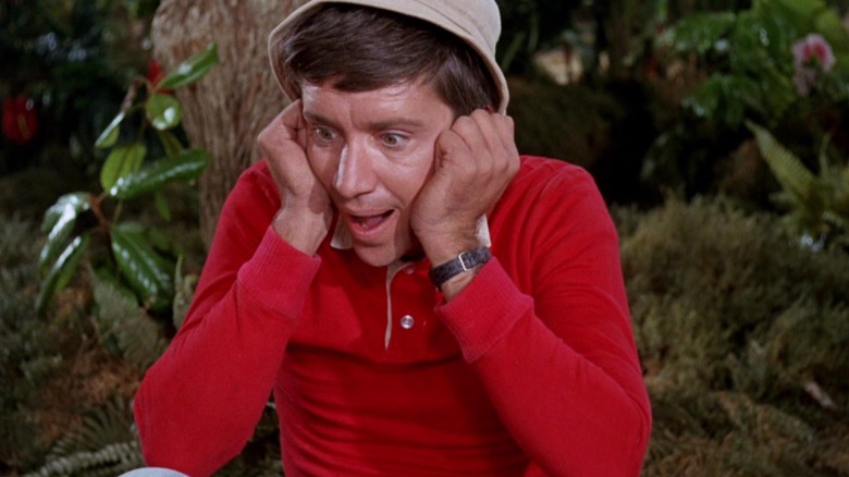 Gilligan, sitting against a palm tree, clasping his face.