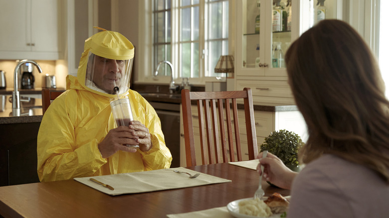 Monk sips a beverage wearing a hazmat suit