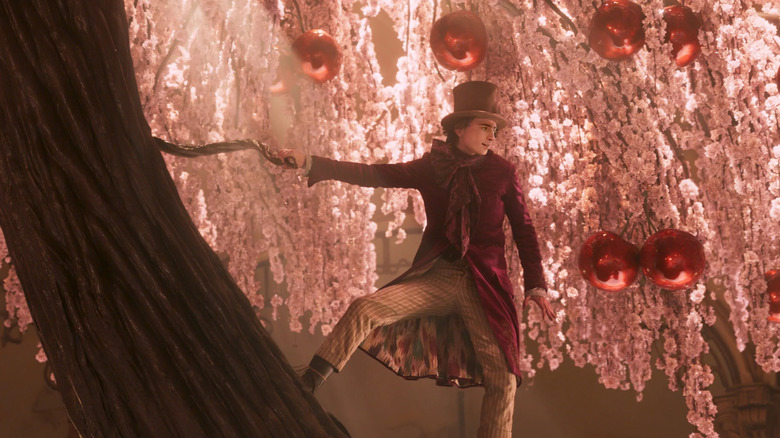 Timothée Chalamet as Willy Wonka, standing on a tree, in Wonka