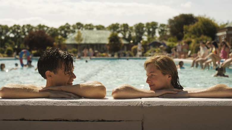 harry styles and emma corrin smiling at one another with their arms resting on the edge of a pool in the movie my policeman