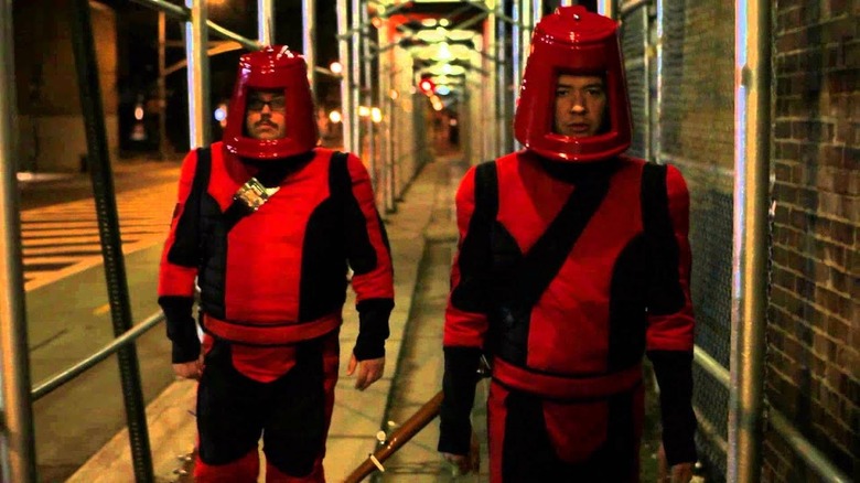 Trius and Kevin walk through New York in red Devo-esque outfits in The History of Future Folk 