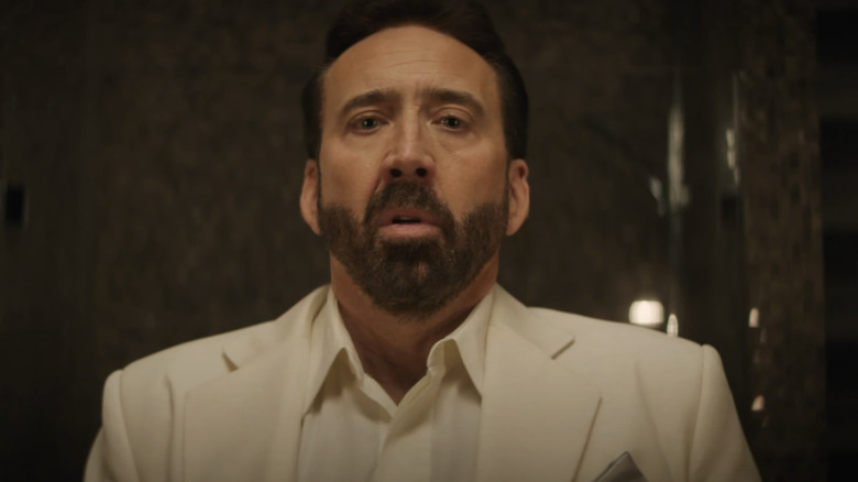 Nicolas Cage's Nick Cage looks disturbed while wearing a white suit in The Unbearable Weight of Massive Talent