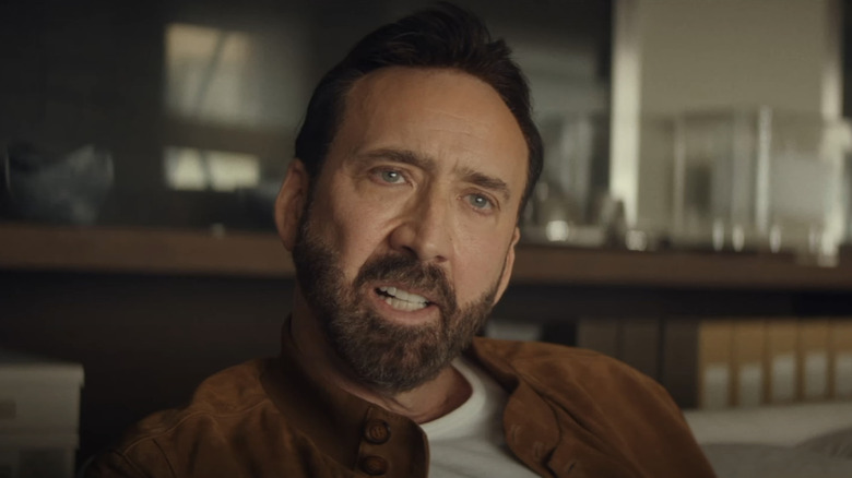 Nicolas Cage's Nick Cage looks across frame while sitting down inside in The Unbearable Weight of Massive Talent