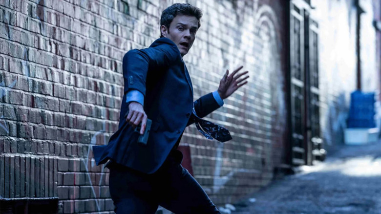 Nathan Caine (Jack Quaid) foge por um beco enquanto segurava uma arma em Novocains