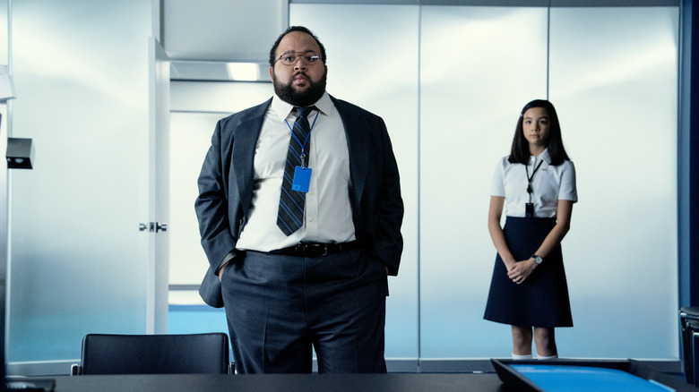 Zach Cherry as Dylan G. and Sarah Bock as Miss Huang standing in Milchick's office in Severance