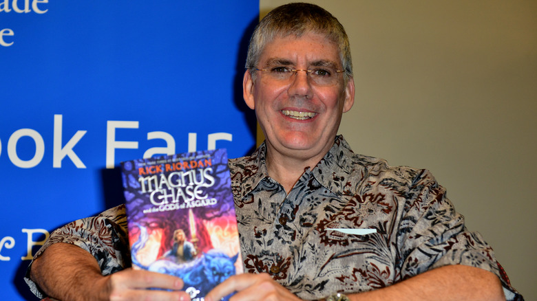 Rick Riordan smiles with copy of Magnus Chase book