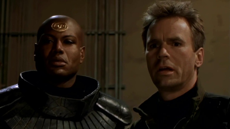 O Jack de Christopher Judge do Juiz e Richard Dean Anderson falando com Hammond em Stargate: SG-1 Filhos dos Deuses