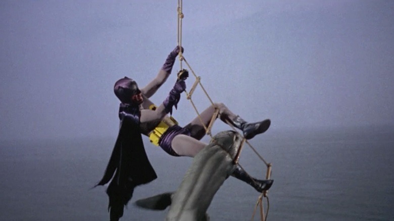 Batman hangs from a ropeladder, a shark hanging from his leg