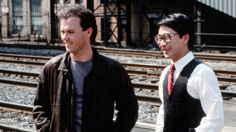 Michael Keaton and Gedde Watanabe stand by railroad tracks