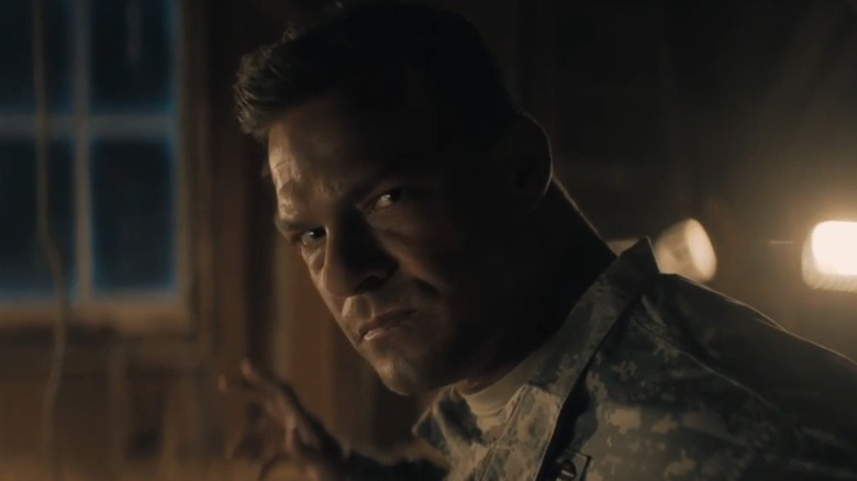 Alan Ritchson's Jack Reacher looks troubled as holds his hands up in Reacher