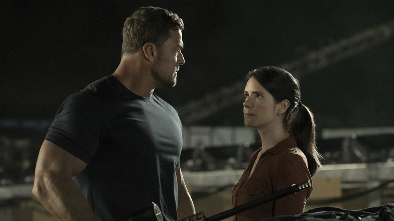 Alan Ritchson's Jack Reacher holds a rifle and stands face to face with Sonya Cassidy's Susan Duffy in Reacher