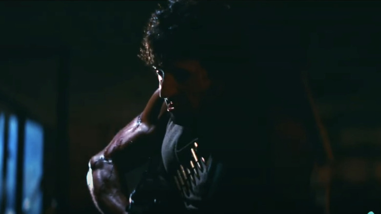 Sylvester Stallone's John Rambo holds a machine gun in a dark room in First Blood