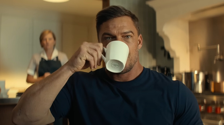 Alan Ritchson como Jack Reacher bebendo uma caneca de café no Reacher