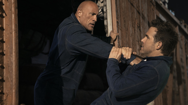 Dwayne Johnson holds Ryan Reynolds out of a train car