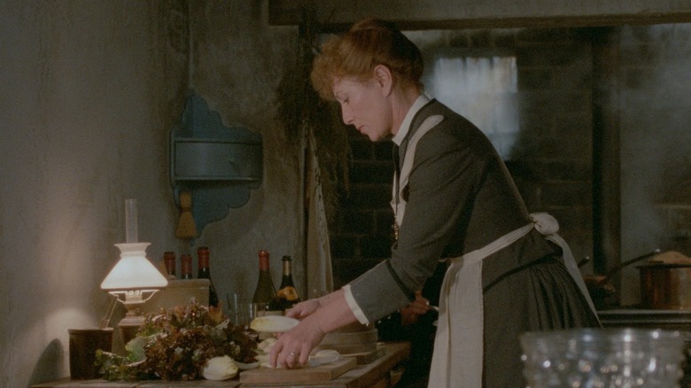 Babette carefully prepares a vegetable dish in a modest kitchen