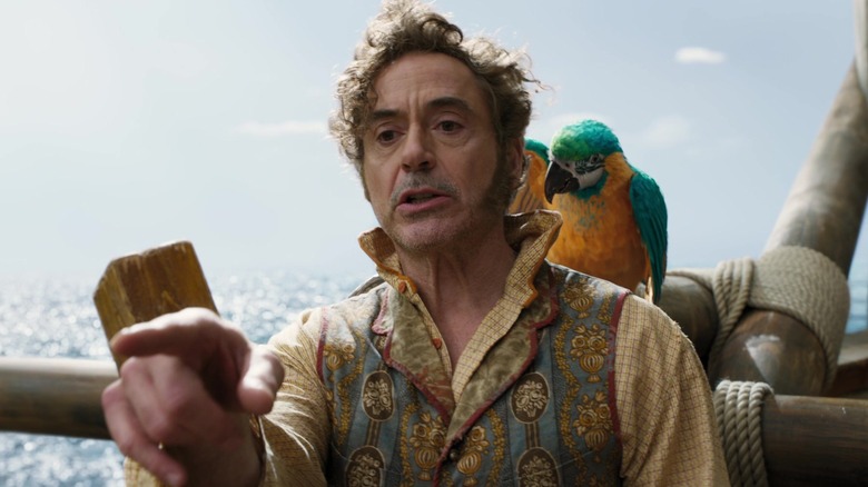 Dr. Dolittle, standing on the deck of a ship, a macaw on his shoulder, pointing at something