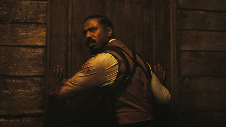 Michael B Jordan looks concerned as he holds a door shut in Sinners