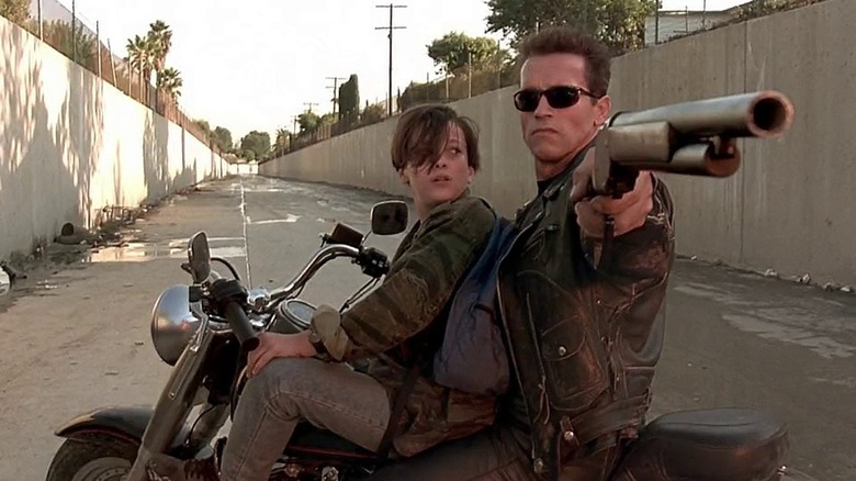 Arnold Schwarzenegger pointing gun on motorcycle, Edward Furlong also seated