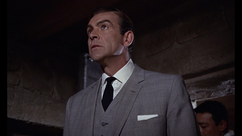 Sean Connery's James Bond is seen from a low angle wearing a grey suit in Goldfinger