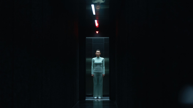 Dichen Lachman as Gemma Scout standing inside an elevator in a darkened hallway in Severance