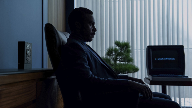 Mr. Milchick wearing a suit, sitting in his office chair in Severance