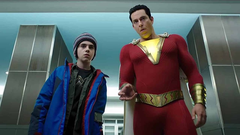 a boy in a blue jacket and winter hat standing next to a man in a red and yellow super suit looking at the camera