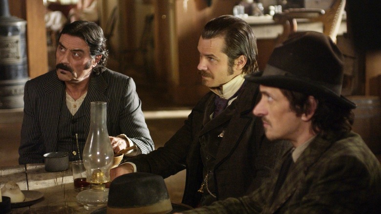 Three men from Deadwood sit at table looking off-screen