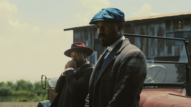 Michael B. Jordan as both of the Smoke brothers leaning against a car in Sinners