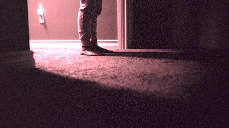 A young boy's feet, standing in a dimly lit hallway at night in Skinamarink