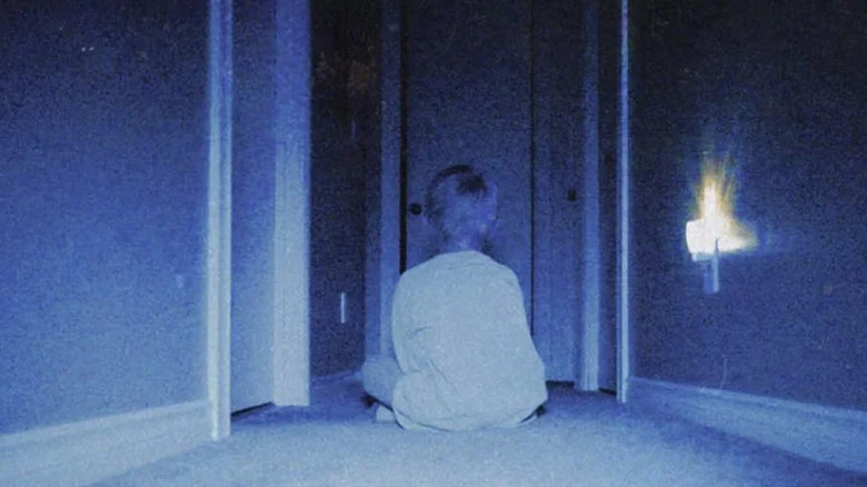 A boy sits cross-legged in a darkened hallway in Skinamarink