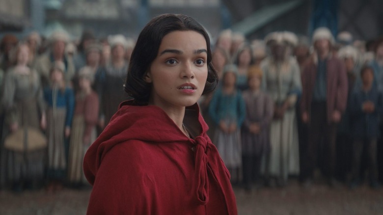 Snow White, in a red cloak, looking intensely at something, a crowd of people behind her. From Snow White.