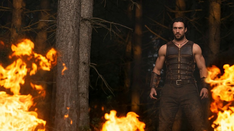 Aaron Taylor-Johnson as Kraven standing in a flaming forest in Kraven the Hunter