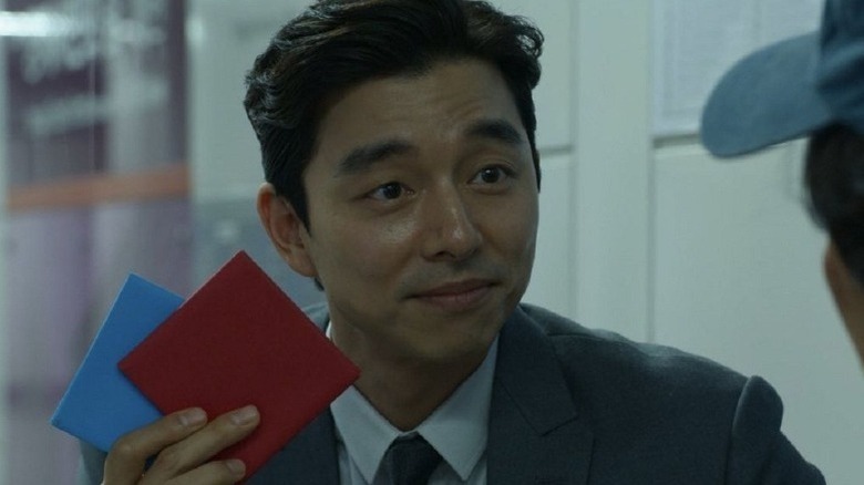 Gong Yoo as The Salesman holding two red and blue Ddakji envelopes