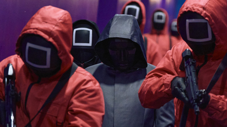 Front man surrounded by pink-suited guards at Squid Game