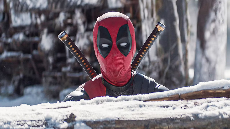 Deadpool, mirando por encima del tronco de un árbol nevado, en Deadpool & Wolverine