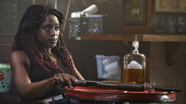 A young guinan sits at a table, looking threatening. A bottle of booze and a shotgun are on the table in front of her.