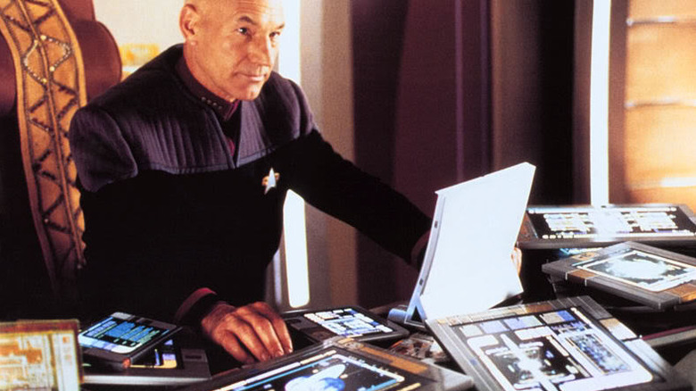 Capitão Picard com um monte de computadores e padds ao seu redor na franquia Star Trek