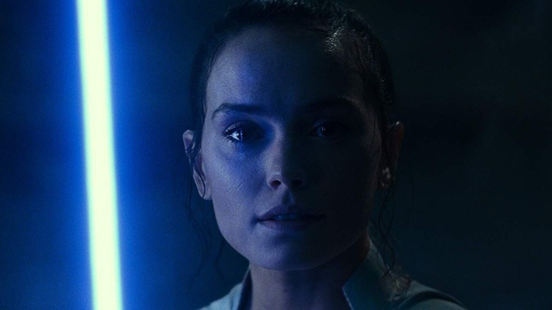 Daisy Ridley Rey holds a blue lightsaber in the film 