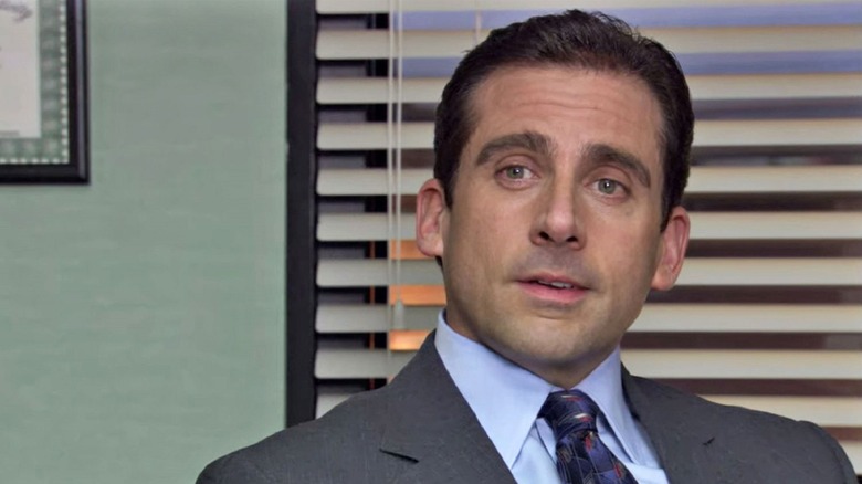 Michael Scott sits on his office and looks at Camerorson outside the screen in the office